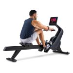 Uomo di schiena sul Vogatore NordicTrack RW300 mentre rema con il display acceso.