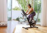 Donna felice si allena su Spin Bike Elettromagnetica Bowflex IC Bike SEi in un moderno soggiorno con giardino