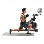 Uomo in affondo con manubri gommati accanto alla Spin Bike NordicTrack S10i