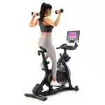 Donna seduta sulla Spin Bike NordicTrack S10i con manubri, per allenamento total body