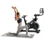 Donna che si allunga su tappetino davanti alla Spin Bike NordicTrack S10i