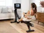 Donna bionda in top e pantaloncini color crema fa canottaggio con il Vogatore NordicTrack RW700 a casa
