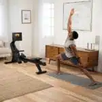 Uomo con maglietta e pantaloncini grigi che pratica yoga vicino al Vogatore NordicTrack RW700, mostrando versatilità fitness