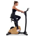 Donna di profilo in abbigliamento sportivo si allena su una Cyclette Spheris 4.0 NorsK