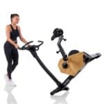 Donna sposta la Cyclette Spheris 4.0 NorsK ripiegata con maniglia, su ruote integrate